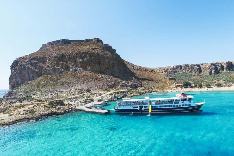 A small tour boat anchored off a rocky headland in clear turquoise water